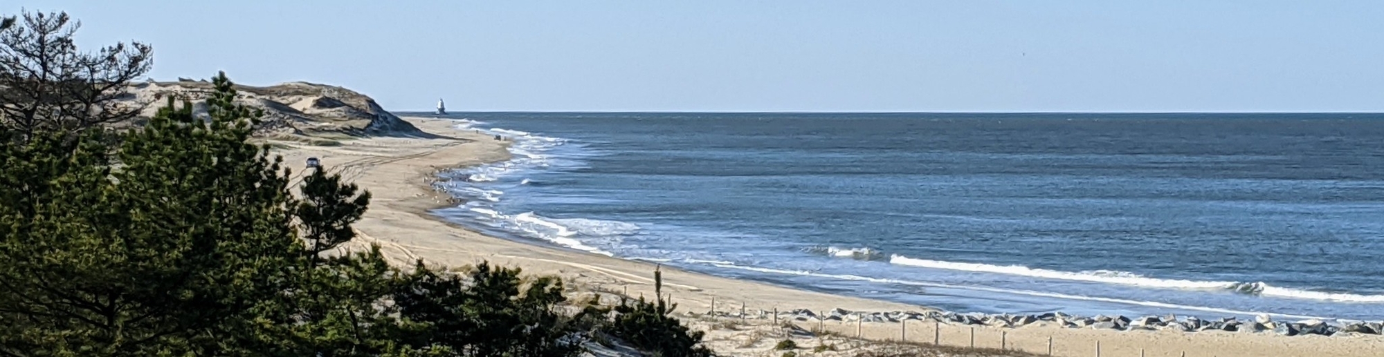 A view of the beach at Cape Henlopen. There's a tall dune on the left and the blue ocean on the right.