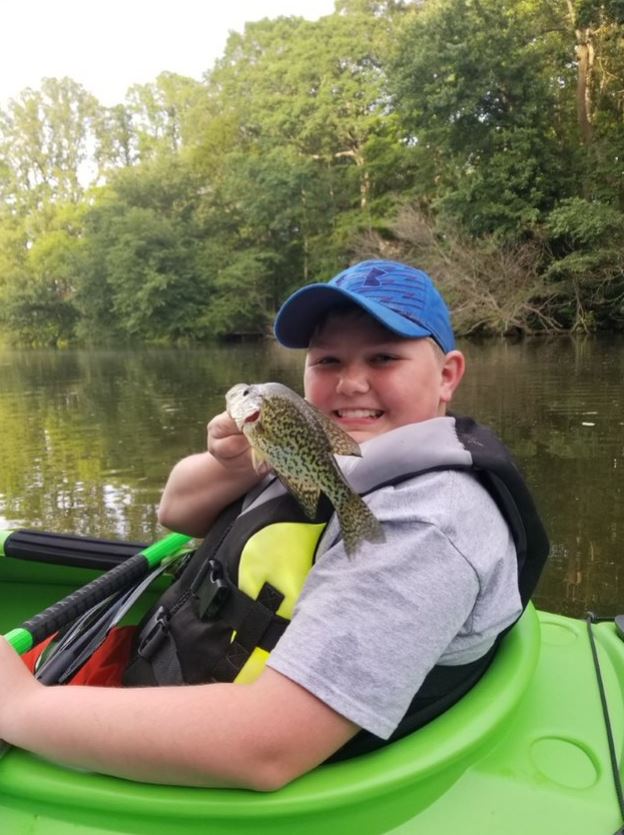 A smiling boy in a kayak holds up a fish.