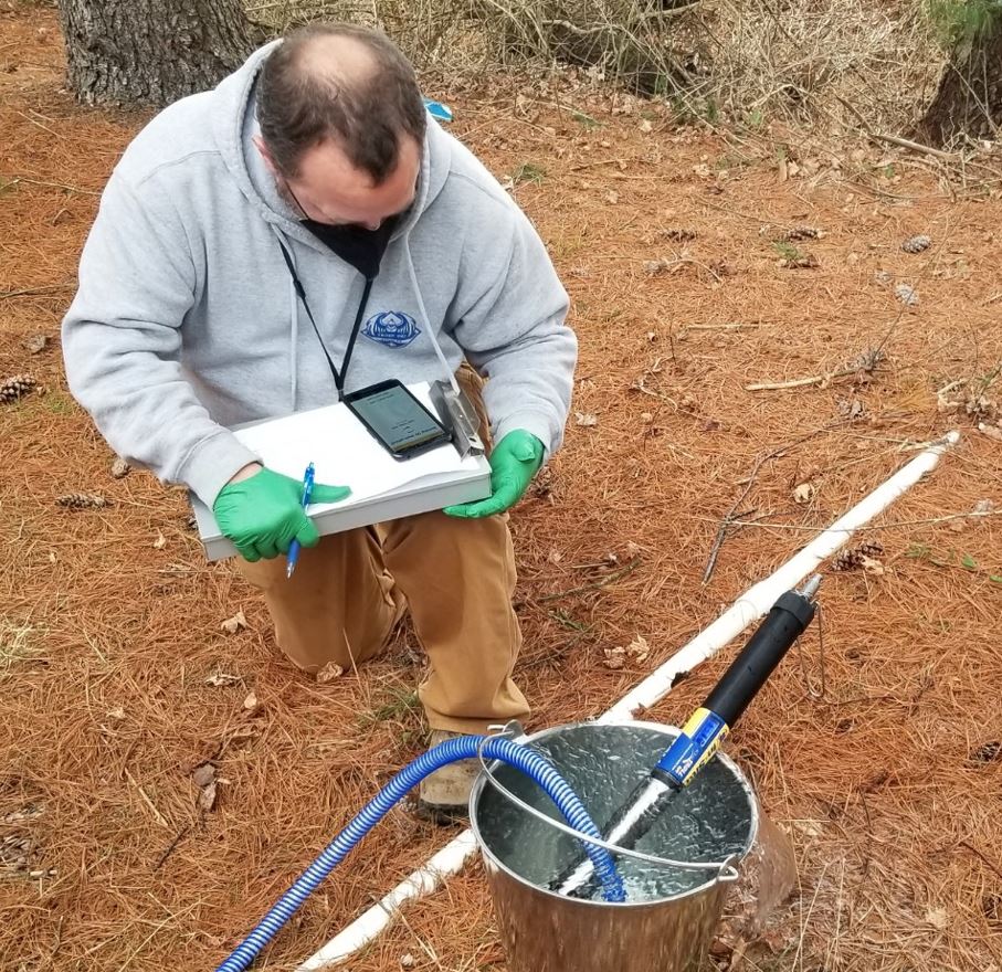 A male scientist, seen from above with a clip-board, takes a reading from instruments outdoors.